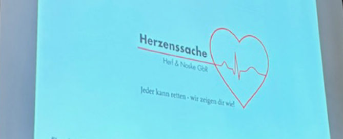 Bei einem 1. Hilfe Kurs produziert ein Videobeamer ein Foto auf eine Leinwand, auf dem das Wort "Herzenssache" steht.