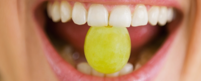 Ein gelbes Bonbon wird im Mund von den Vorderzähnen gehalten.